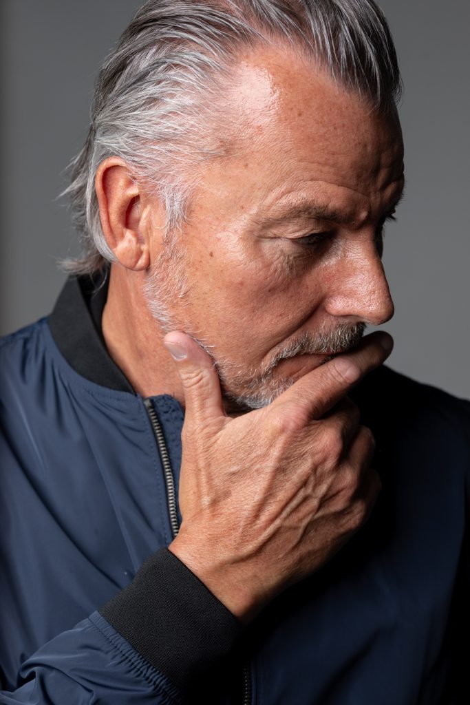 A man with grey hair is holding his chin.