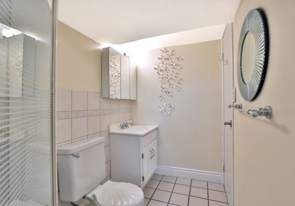 A bathroom with white tile and a toilet, sink, mirror and cabinet.